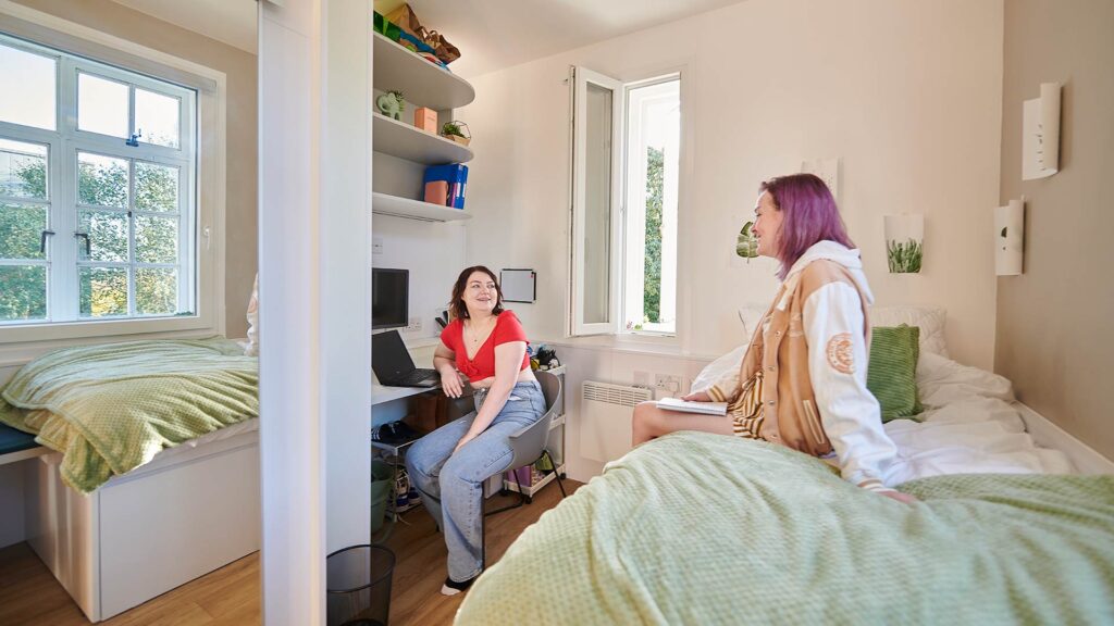 Two girls chatting in a room in halls on campus.