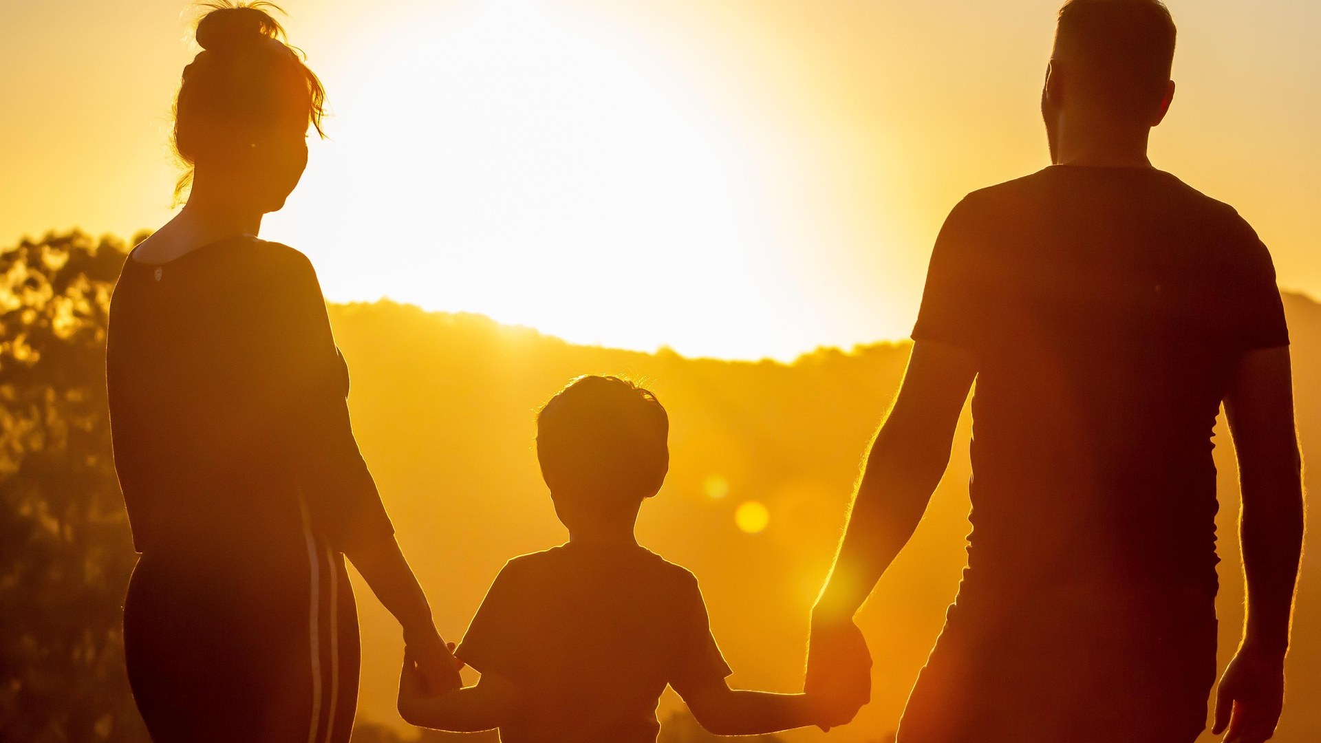 A family walk towards the horizon holding hands with a child in the middle